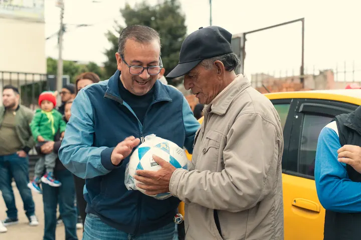 Doryan Jara entrega un balón a un adulto mayor en una calle de Riobamba.
